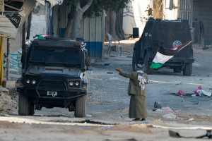 A man holding a Palestinian flag gestures next to a vehicle of Palestinian security forces amid clashes with militants at the camp, in Jenin, northern Samaria, December 14, 2024. REUTERS/Raneen Sawafta