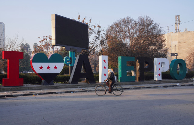 A man on a bicycle passes by a sign reading "I love Aleppo," adorned with flags representing the new Syrian opposition, in Aleppo, Syria, January 8, 2025. REUTERS/Karam al-Masri