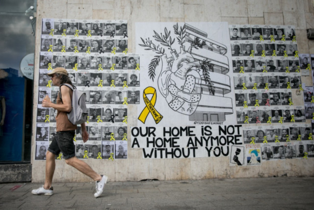Israelis walk past a mural photographs of Israelis held hostage by Hamas terrorists in Gaza since the October 7 massacre, on Dizengoff  in Tel Aviv. The mural was designed by street artists Hastickeriot and Yiddish Feminist. June 23, 2024 (Photo by Miriam Alster/FLASH90).
