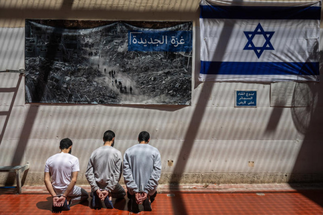 Handcuffed Hamas terrorists sit next to a picture of Palestinians walking past destroyed buildings in the Gaza Strip and an Israeli flag, in a prison in central Israel, May 6, 2025. Photo by Chaim Goldberg/Flash90