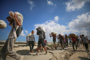 Displaced Palestinians carry food parcels and supplies from a GHF aid distribution point at the “Netzarim corridor” in the central Gaza, August 5, 2025. Photo by Ali Hassan/Flash90