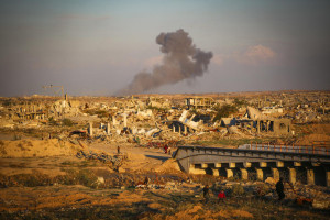 Palestinians walk in the street as smoke rises following an Israeli airstrike in Gaza City, December 2, 2025. Photo by Ali Hassan/Flash90