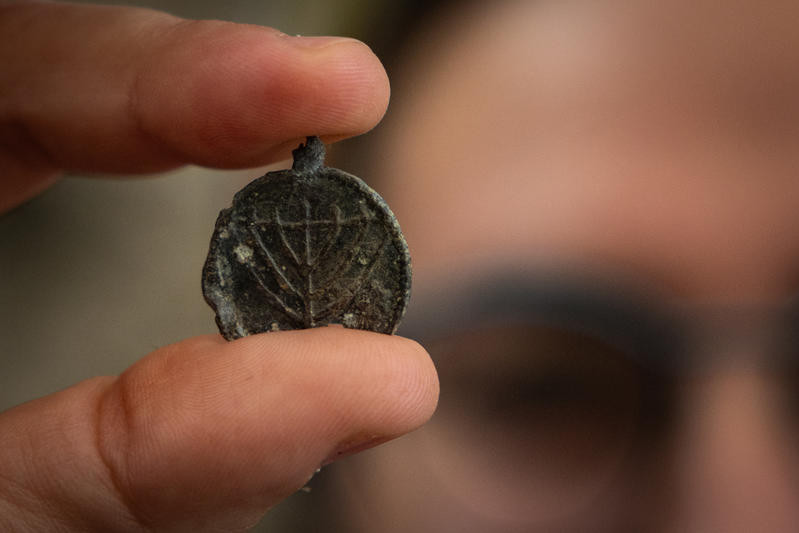 An Israeli Antiquities Authority (IAA) archaeologist holds a a 1,300-year-old menorah-decorated pendant discovered during an Israel Antiquities Authority archaeological excavation near the Western Wall in Jerusalem’s Old City, December 15, 2025. Photo by Yonatan Sindel/Flash90